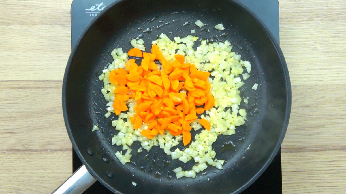 Black frying pan with minced onion, garlic, and a small heap of carrot pieces.