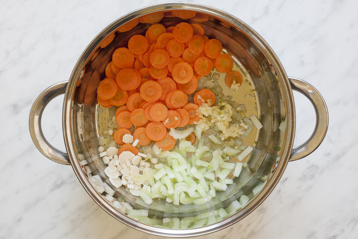 Stockpot with minced onion, carrot slices, celery slices, and parsnip slices.