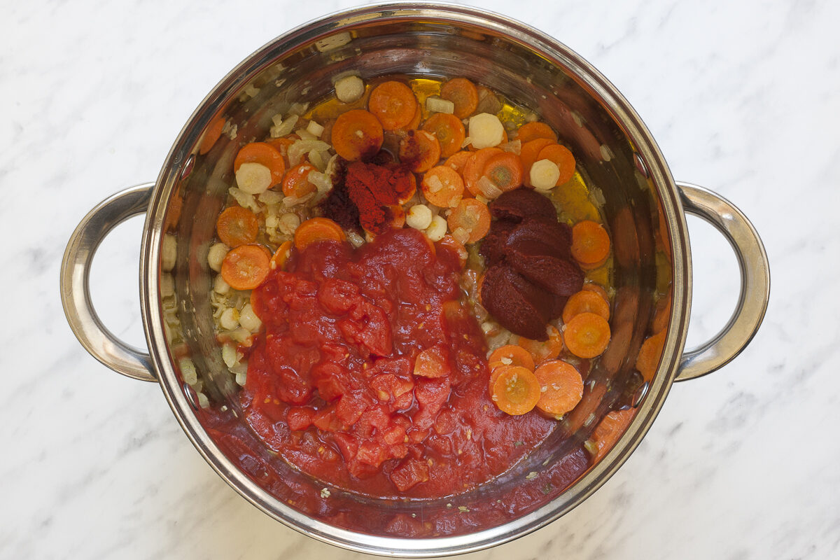 Stockpot with carrot, celery, and parsnip slices with a large heap of tomato sauce, paste and paprika powder