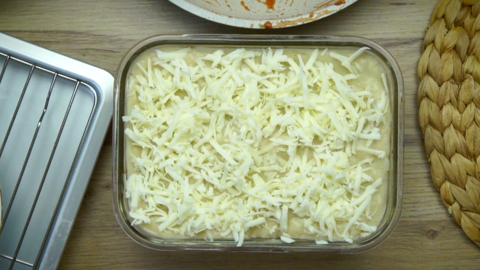 A greased rectangular glass baking dish with light yellow sauce and shredded cheese.