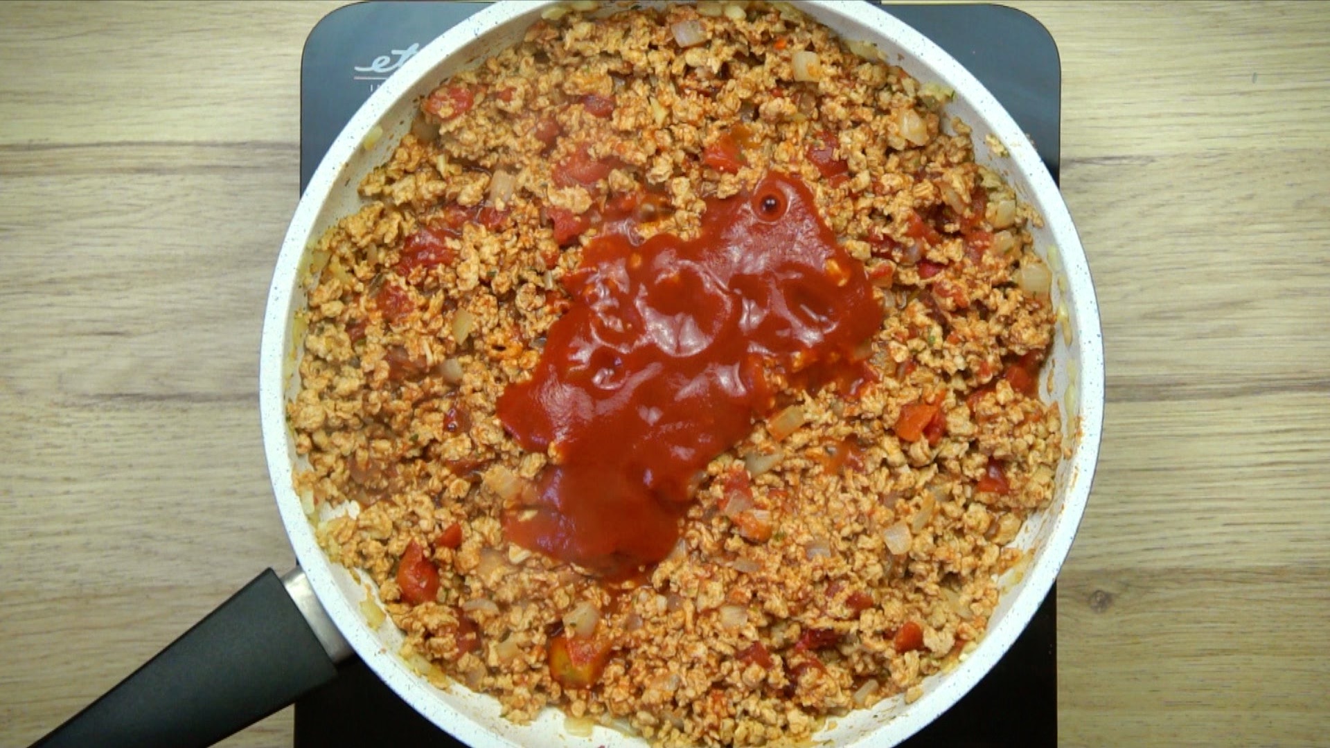 White frying pan with light brown crumbles with a heap of tomato sauce.