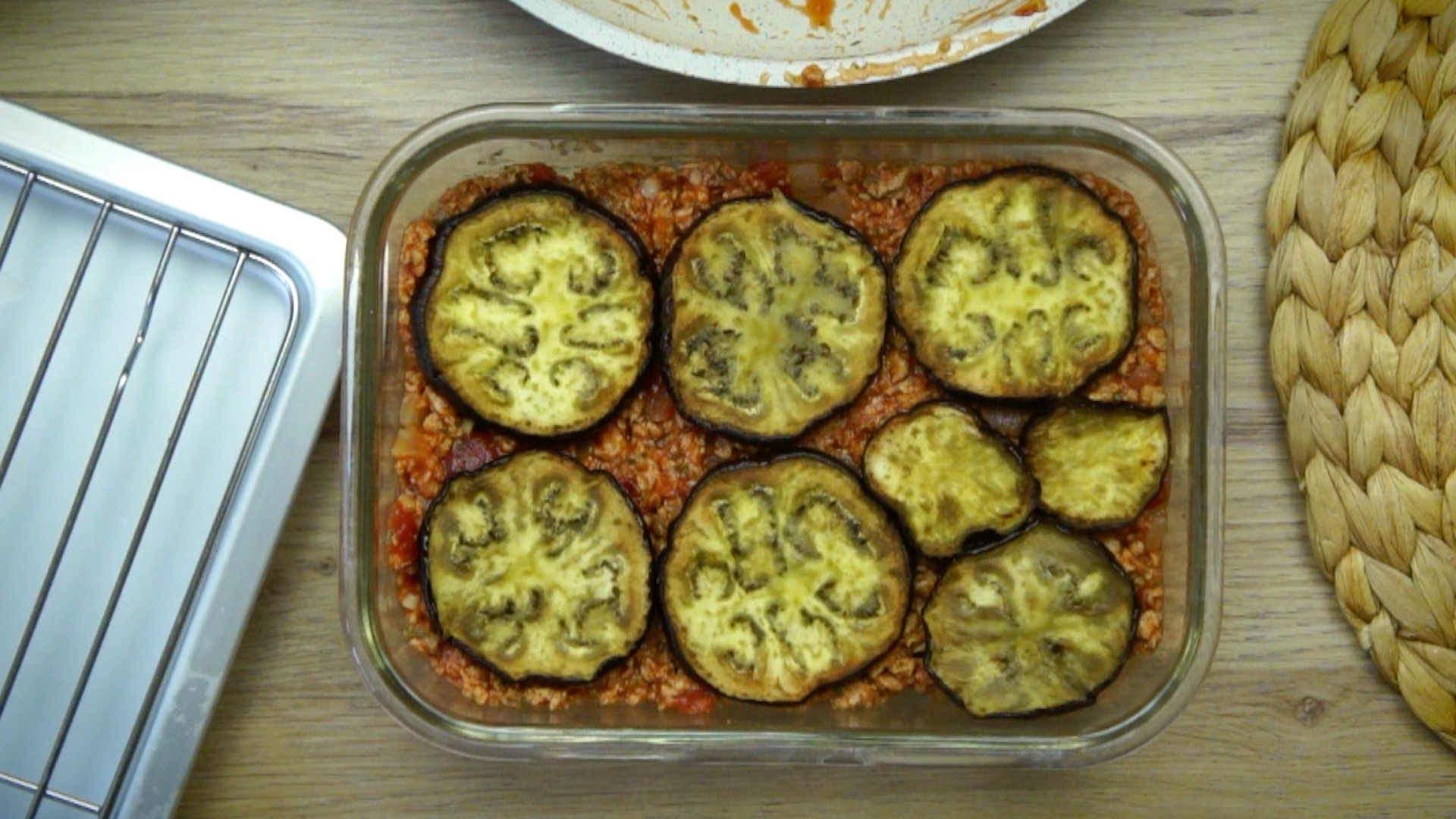 A greased rectangular glass baking dish with brown crumbles and fried eggplant slices on top.