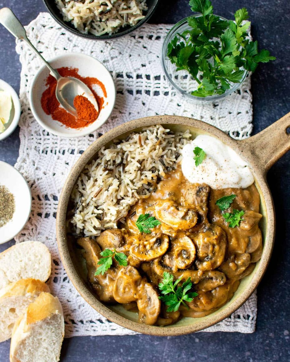 A large brown bowl from above with mushroom slices in a dark brown sauce served with white and wild rice mix.