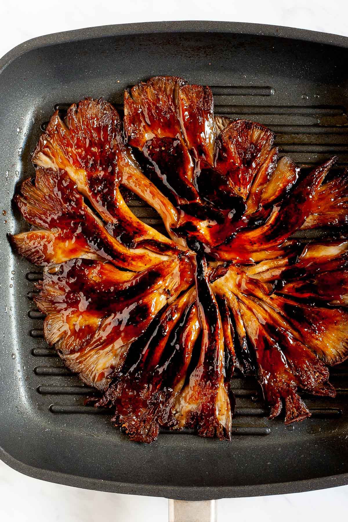 Black grill pan from above with crispy dark brown juicy flattened oyster mushroom clusters