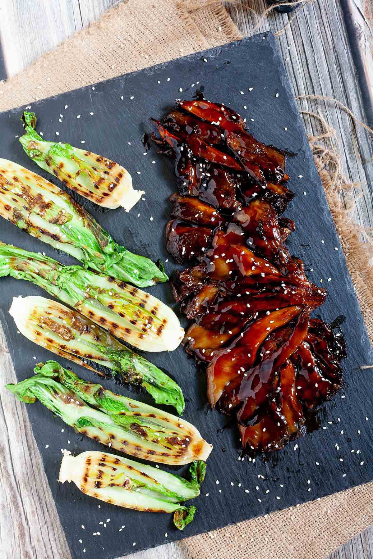 Black board above with crispy brown juicy flattened oyster mushroom clusters and half bok choy with charcoal stripes