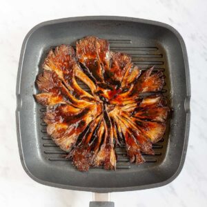 Black grill pan from above with crispy dark brown juicy flattened oyster mushroom clusters