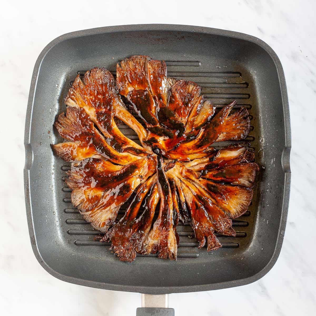 Black grill pan from above with crispy dark brown juicy flattened oyster mushroom clusters