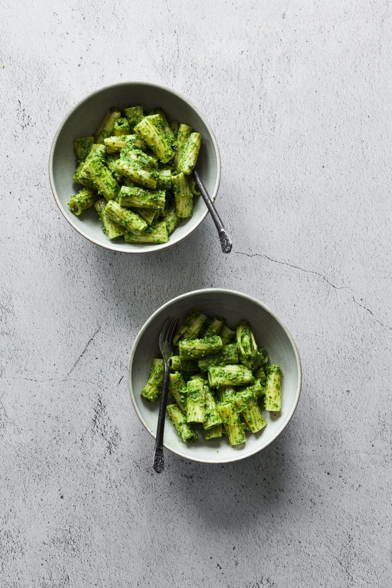 Two small white bowl with penne in a green pesto sauce