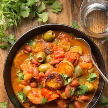 Black bowl of orange stew with olives, plantain slices, bell pepper and kidney beans