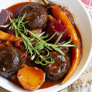 White plate with yellow, red, purple veggies and portobello mushroom caps topped with fresh green herbs on twigs