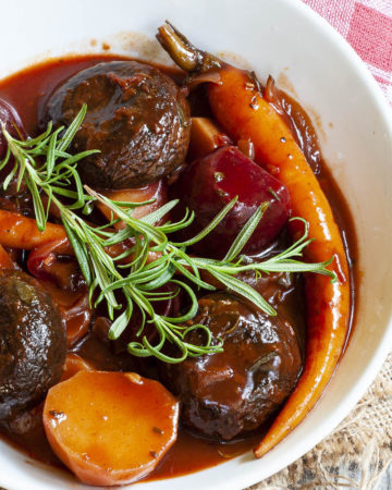 White plate with yellow, red, purple veggies and portobello mushroom caps topped with fresh green herbs on twigs