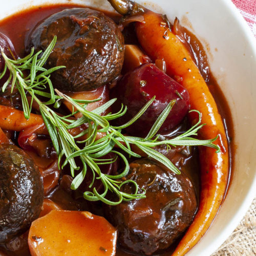 White plate with yellow, red, purple veggies and portobello mushroom caps topped with fresh green herbs on twigs