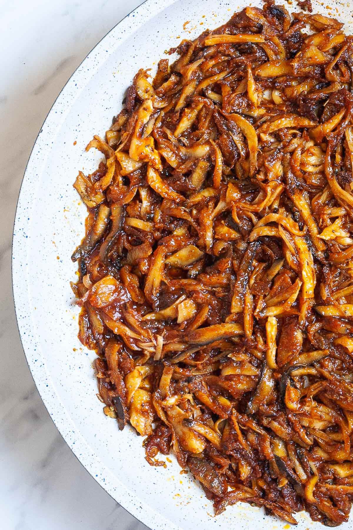 A white frying pan from above with juicy dark brown oyster mushroom shreds.