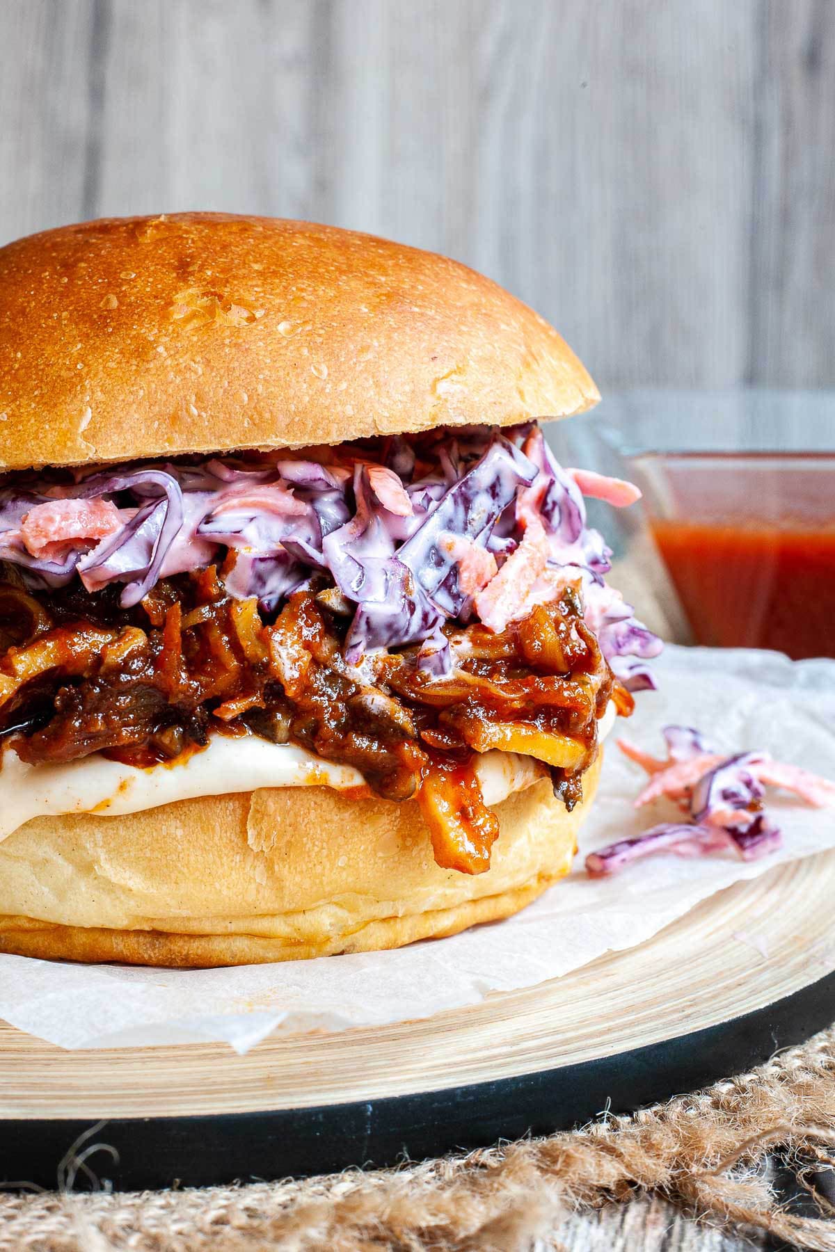 A burger sandwich on a wooden board with white sauce, brown juicy strips and purple cabbage coleslaw.