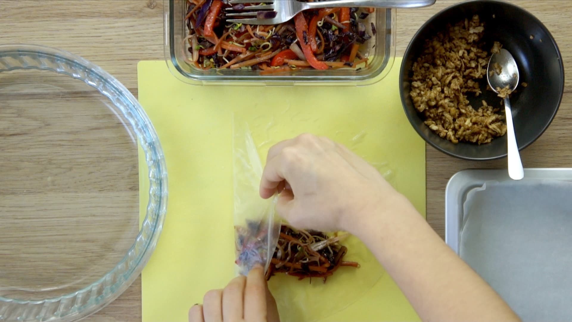 A hand is folding the left side of the rice paper over half of the filling. The fillings are in small bowls next to it.
