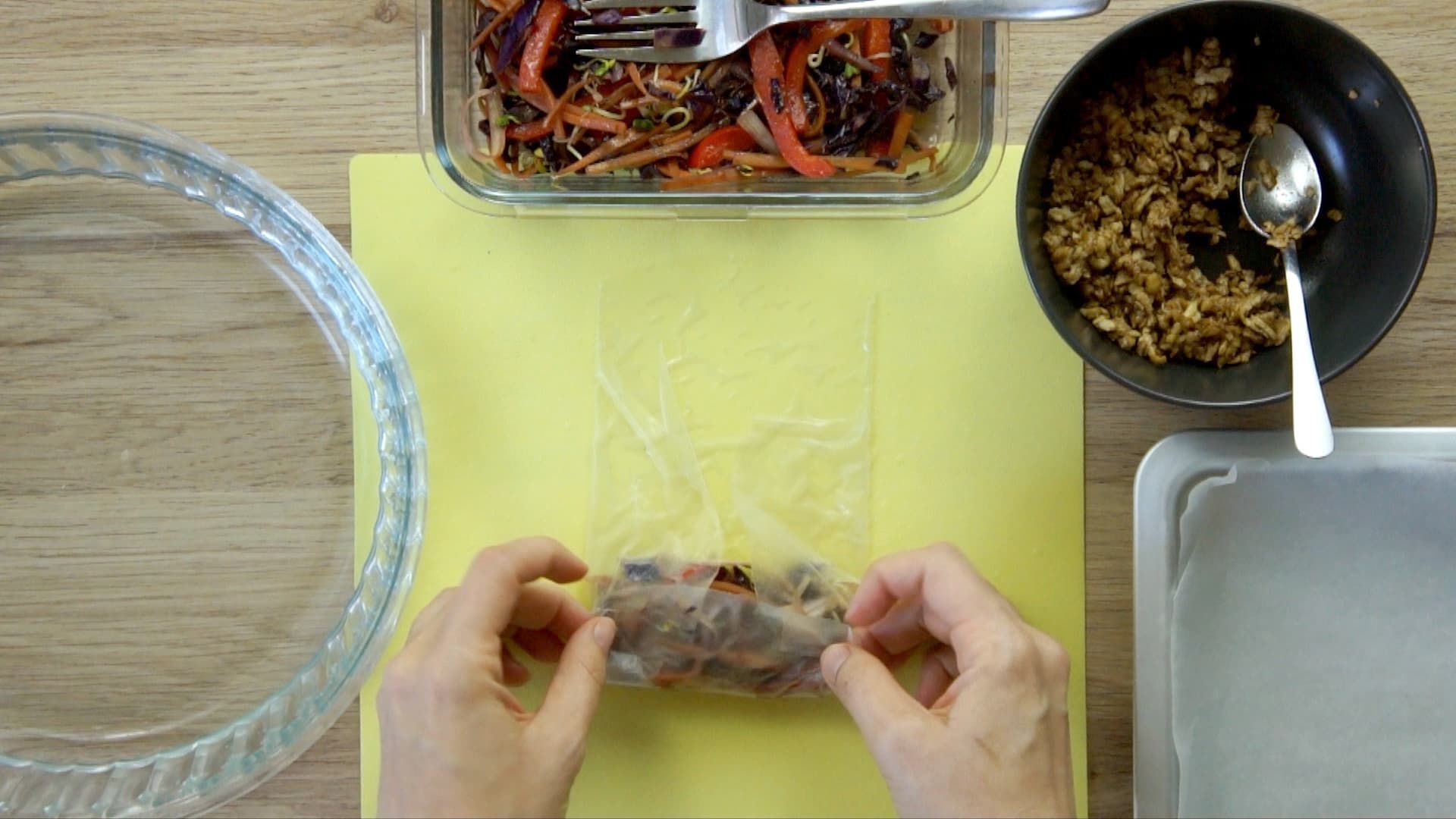 A hand is folding the right side of the rice paper over half of the filling and starts to roll it up. The fillings are in small bowls next to it.