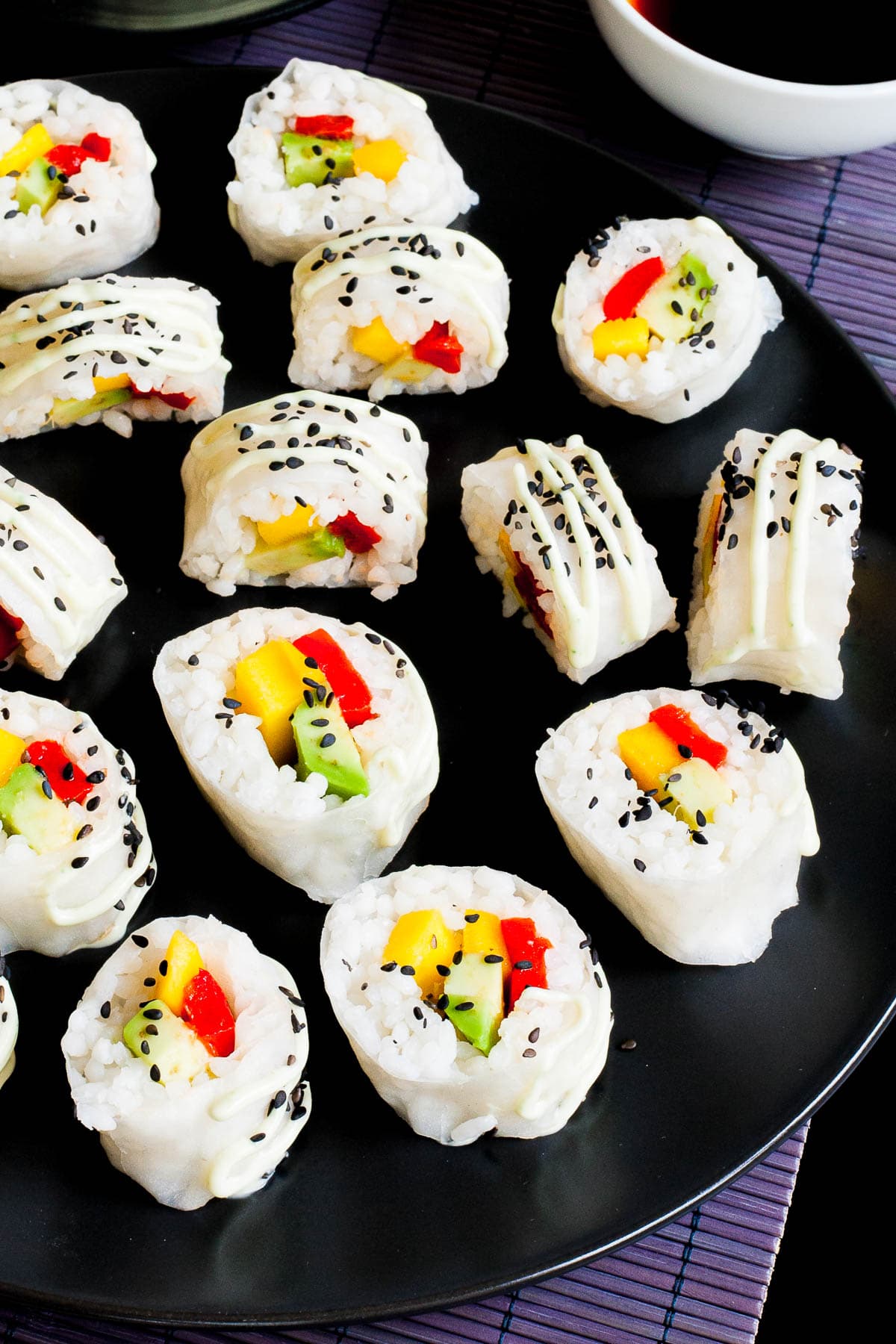 Large black round plate with a lot of white sushi rolls with colorful filling sprinkled with tiny black sesame seeds.