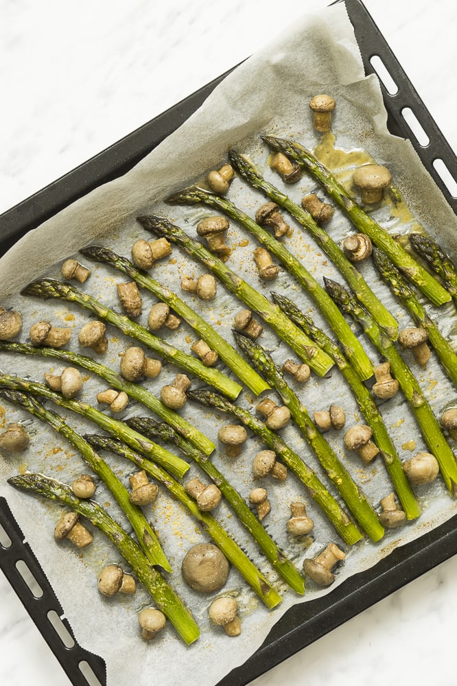 Best spring side dish with asparagus and mushrooms roasted in the oven and ready in under 20 minutes. Easy, delicious and suitable for all diets (vegan, paleo, gluten-free, whole30, keto). #roastedasparagus #asparagusandmushrooms #roastedmushrooms #asparausrecipe #roastedveggies Black sheet pan full of roasted asparagus spears and small champion mushrooms on parchment paper