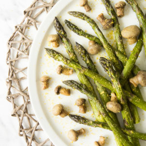 White round plate from above with green asparagus scattered around in between button mushrooms. It is sprinkled with yellow powder.