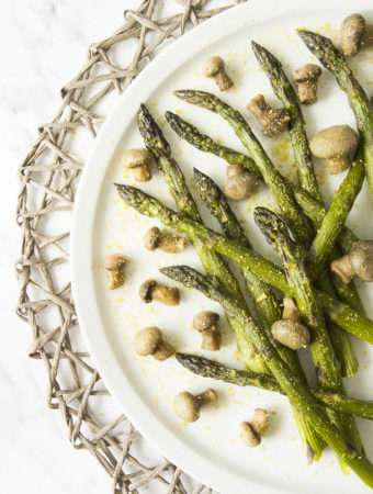 White plate with roasted asparagus and mushrooms styled as messy sprinkled with extra seasoning