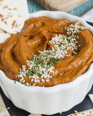 Deep orange brownish cream in a small white bowl topped with green dried herbs and tiny white sees