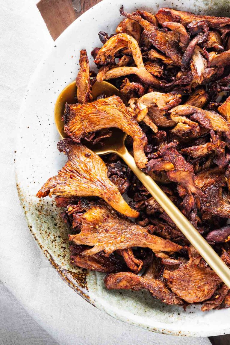 Fried mushrooms in a white bowl with a gold spoon.