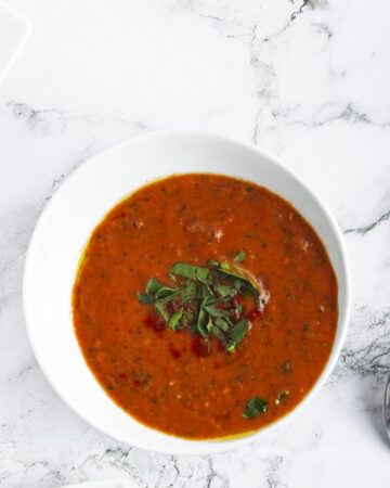 Red soup topped with chopped basil in a white bowl.