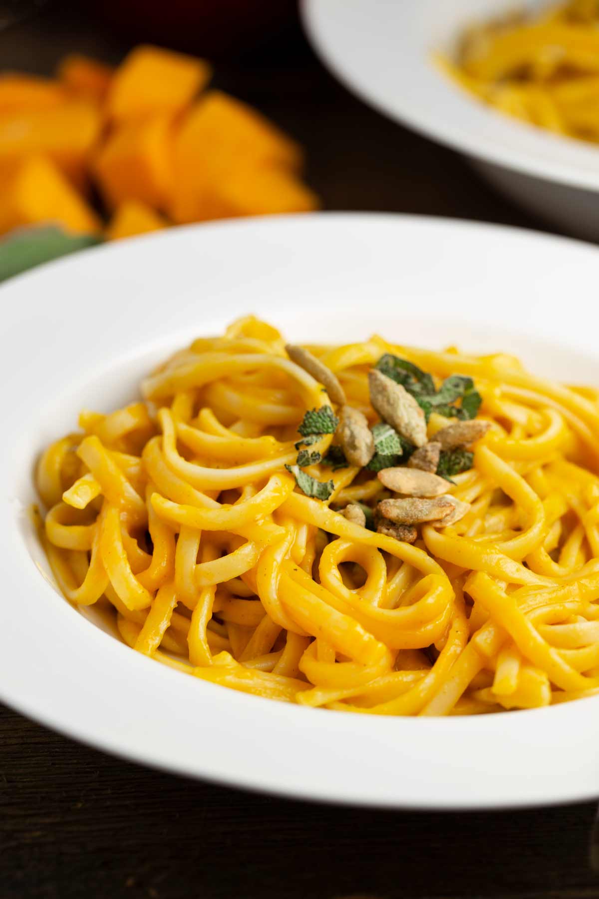 White plate with spaghetti in orange sauce topped with seeds and chopped herbs