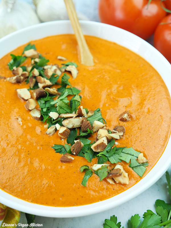 White bowl with orange sauce topped with chopped nuts and herbs