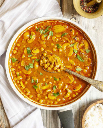 Large saucepan from above with brown-yellow liquid chickpeas and mushroom slices sprinkled with chopped green leaves