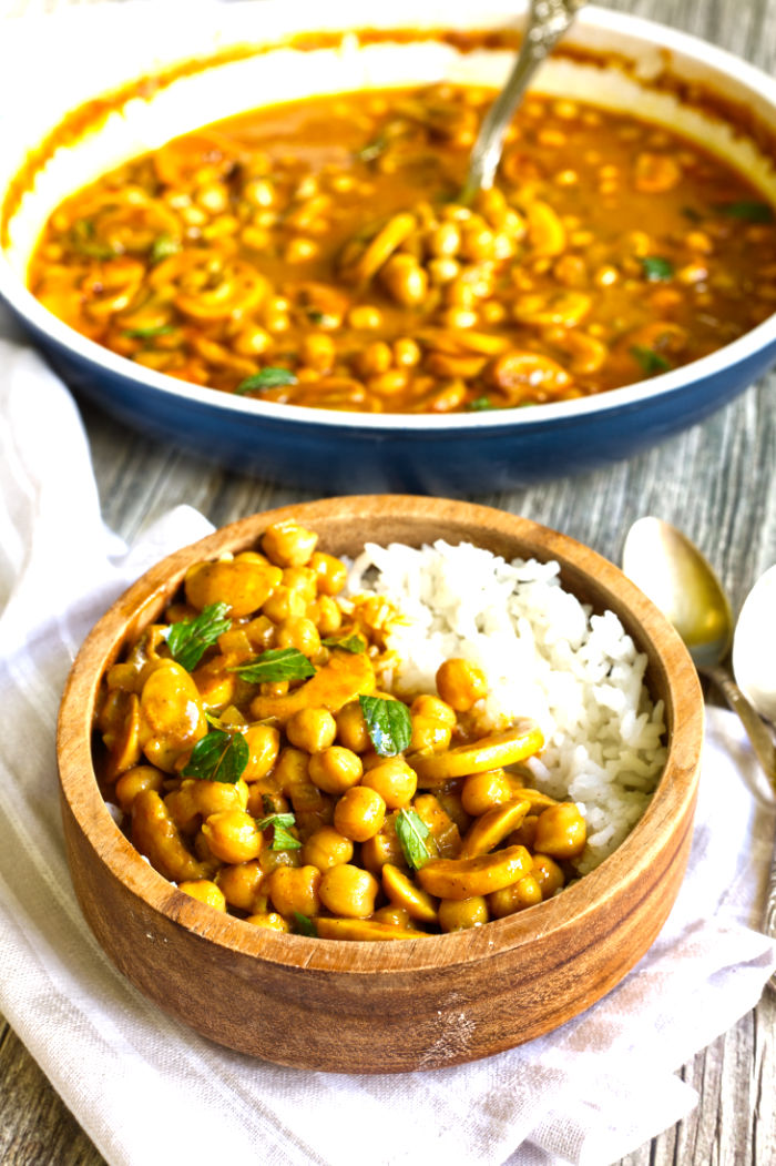 Wooden bowl with rice and chickpeas and mushroom slices in a brown-yellow sauce topped with chopped green herbs
