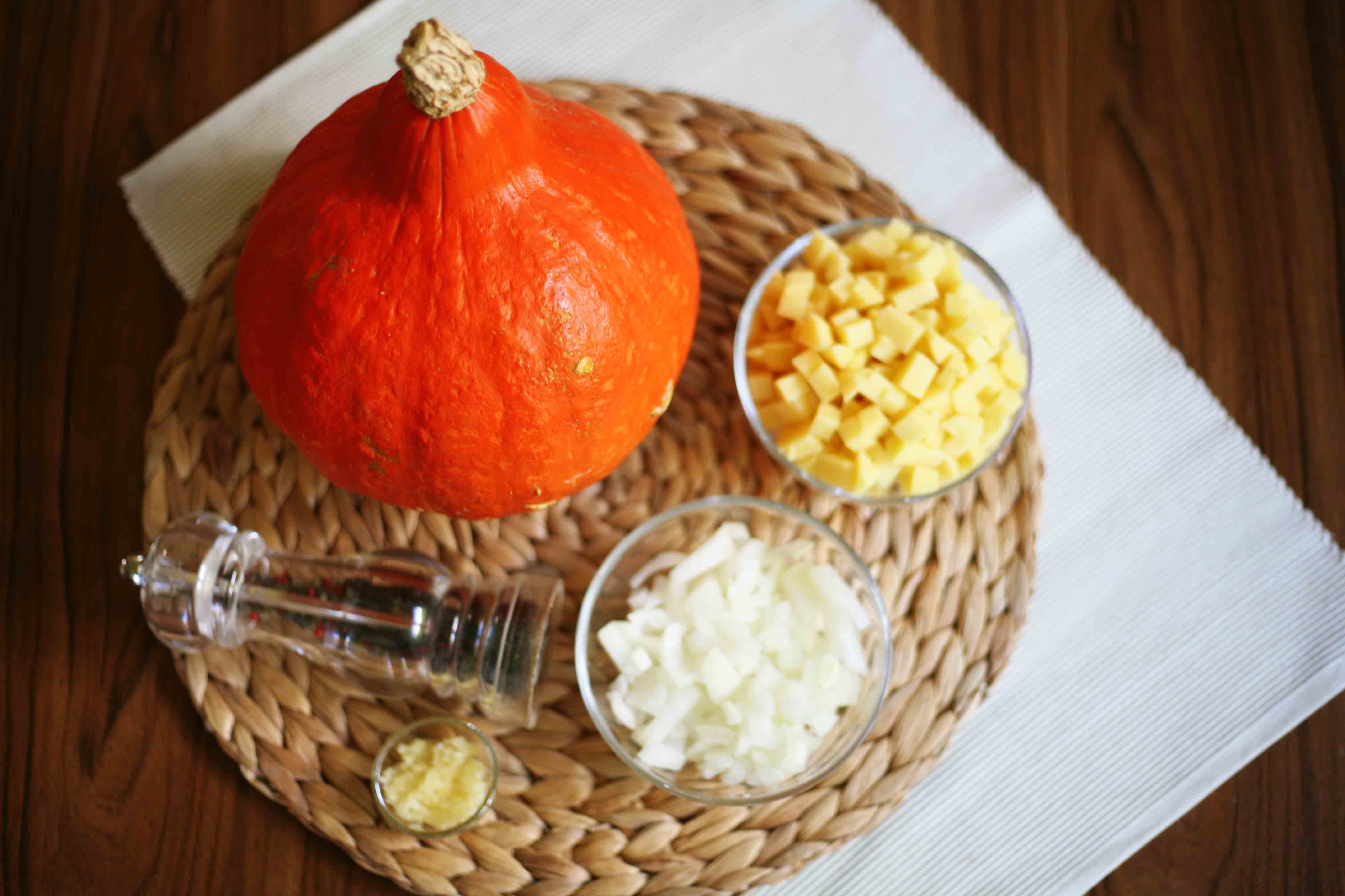 Red squash, diced yellow potatoes in a glass bowl, chopped onion in a glass bowl, chopped garlic in a glass bowl