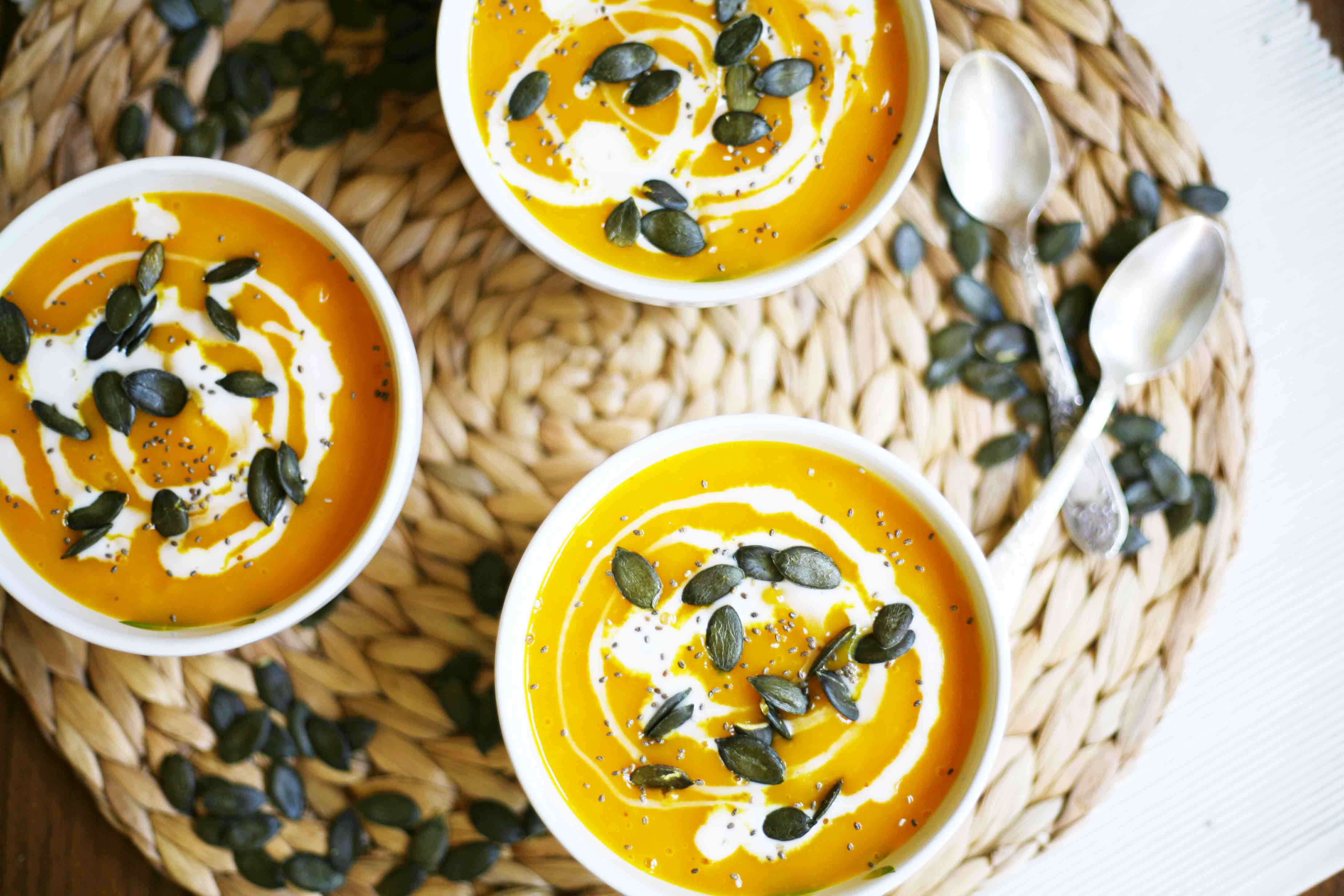 3 small white bowls from above with orange soup topped with pumpkin seeds and a swirl of white sauce