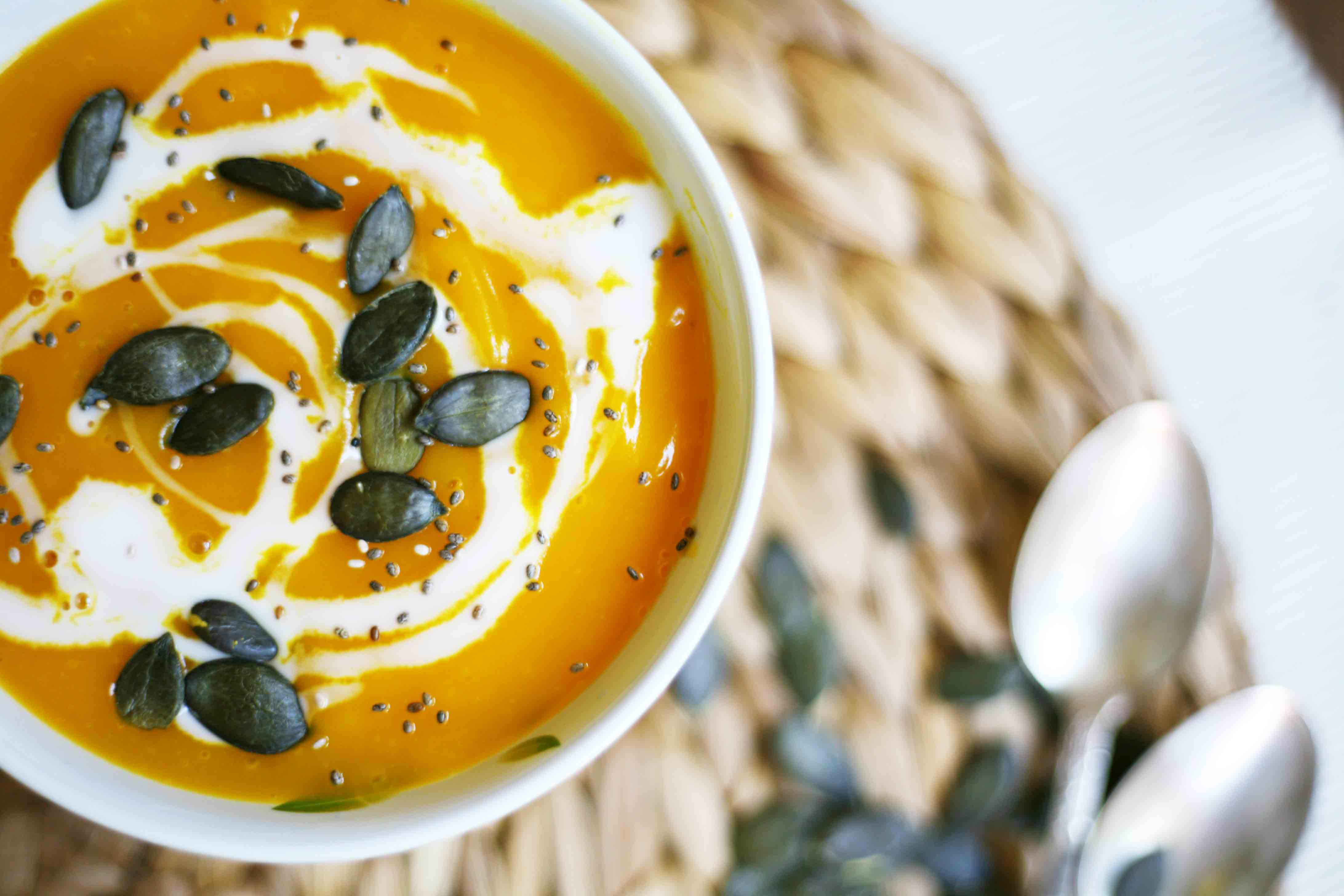A small white bowl from above with orange soup topped with pumpkin seeds and a swirl of white sauce