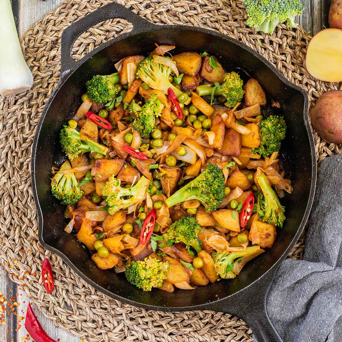 Skillet with potatoes, broccoli, chili peppers, green peas and onion. All slightly fried around the edges.