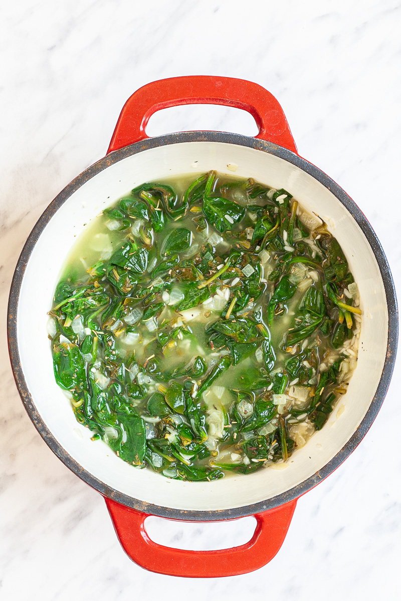 Wilted spinach leaves and sauteed onions in a red white enameled Dutch oven submered in thin broth.