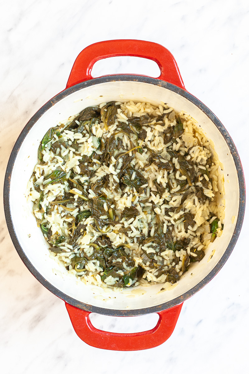 Rice, wilted spinach in an enameled red white Dutch oven.