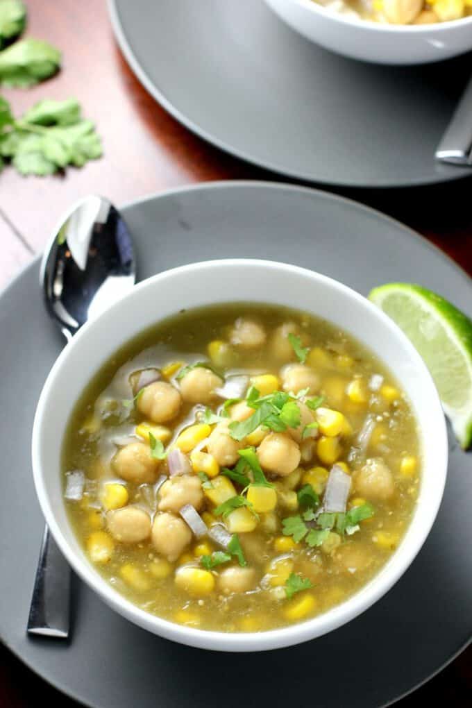 White bowl with a green-yellow stew. Chickpeas, corn and chopped onion is visible.