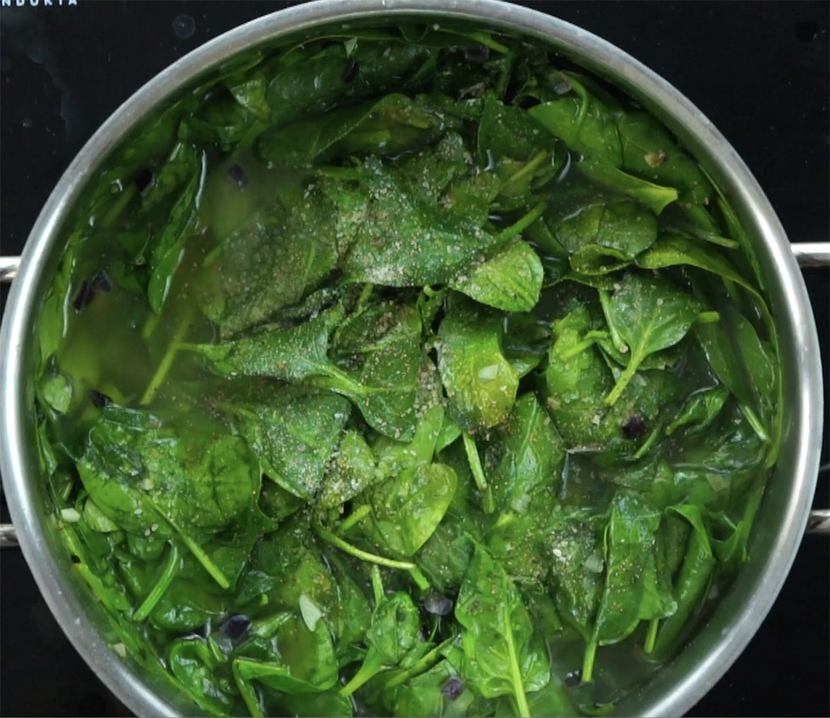 Stockpot with wilted spinach leaves in thin liquid.