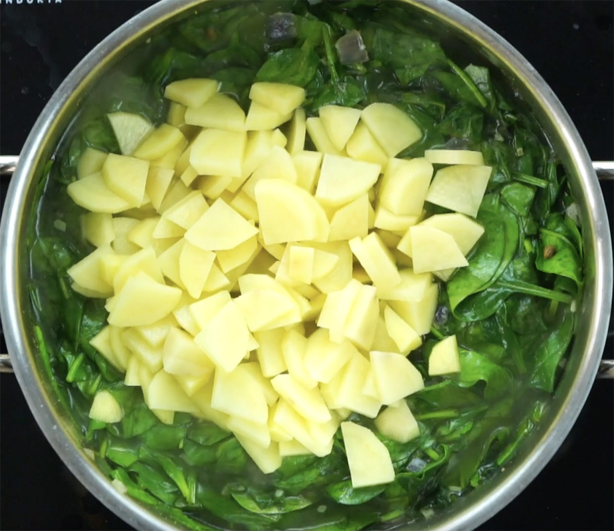 Stockpot with wilted spinach leaves in liquid topped with diced potatoes