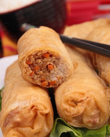 3 spring rolls on a white plate, one is cut to see the filling.