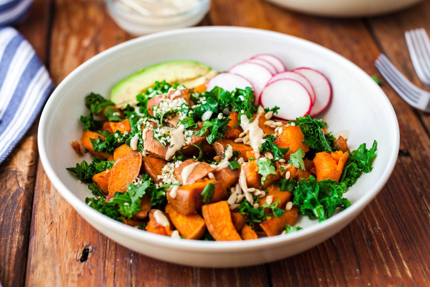 A white bowl of diced sweet potato, kale, radish slices, and avocado.