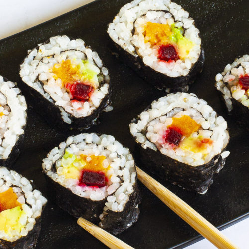 6 sushi rolls on a black plate. The rolls have black cover and white inside with purple yellow and green in the middle.