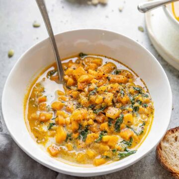 Vibrant yellow creamy sweet potato and kale stew in a white bowl topped with freshly chopped green herbs.