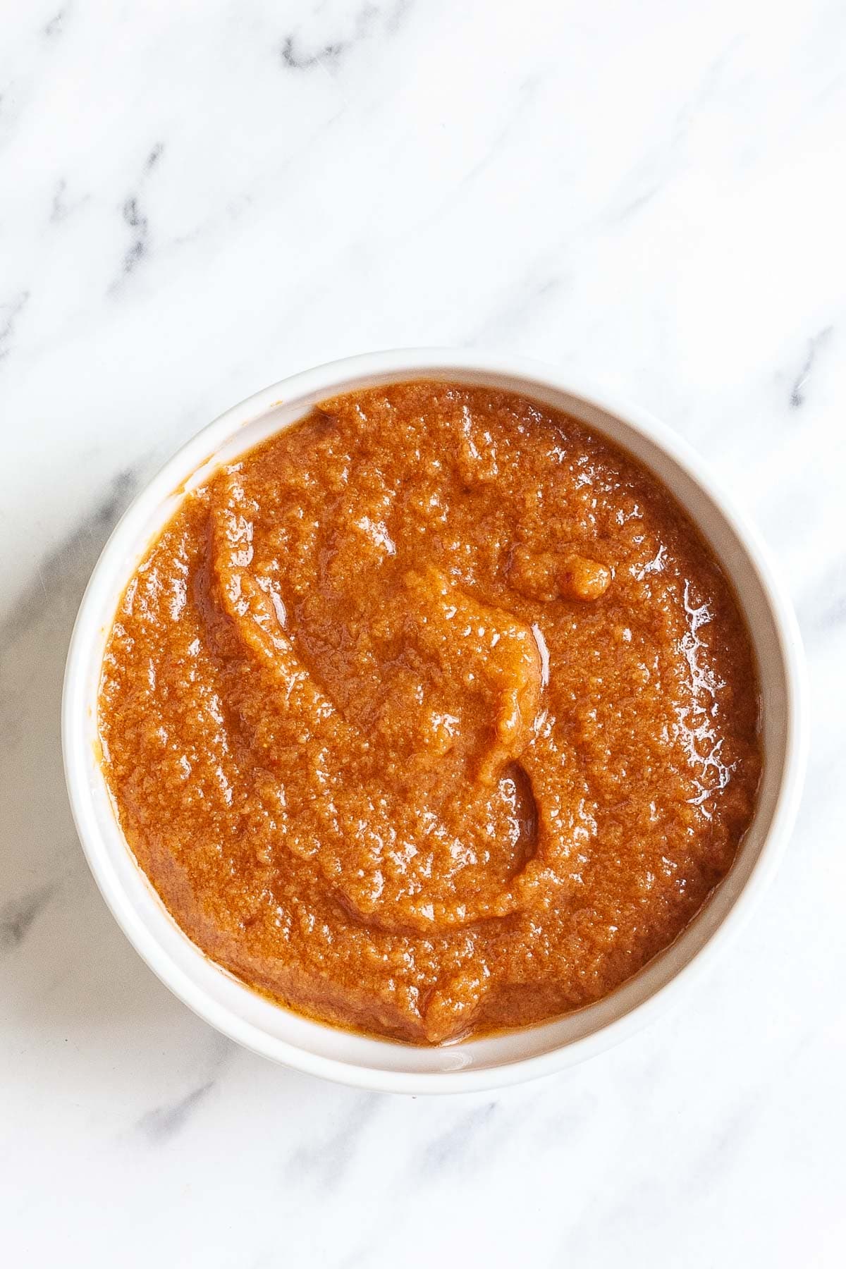 White bowl in red orange thick sauce without any visible ingredients.