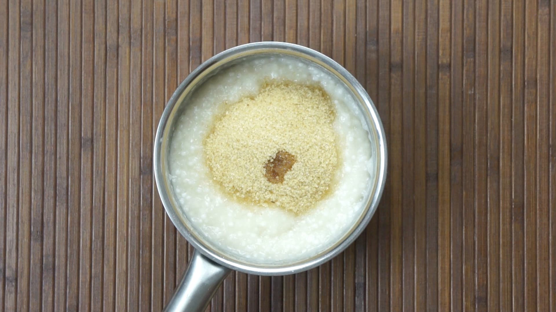 A saucepan on an induction hot plate with a thick white liquid (milk) and small pearls topped with cane sugar and a bit of vanilla extract