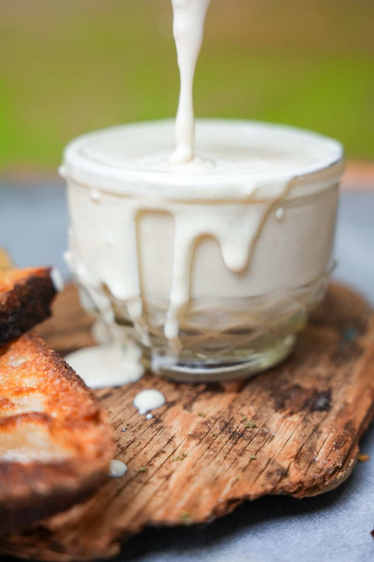 Tarator being poured into a glass. The glass filled up to the bring, and tahini is dripping down the sides. Grilled bread on the side.
