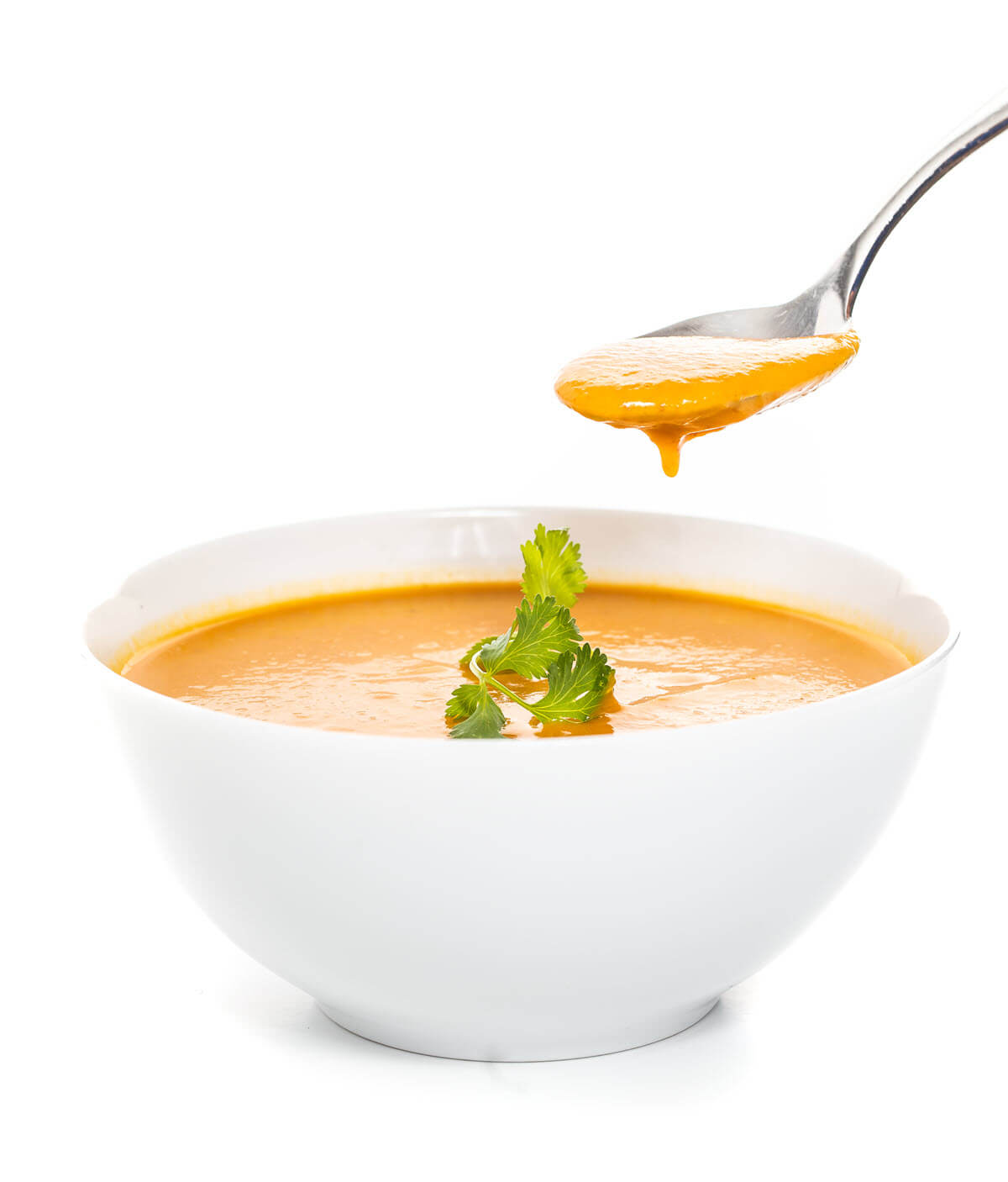 A white bowl with orange soup. A spoon is taking some.