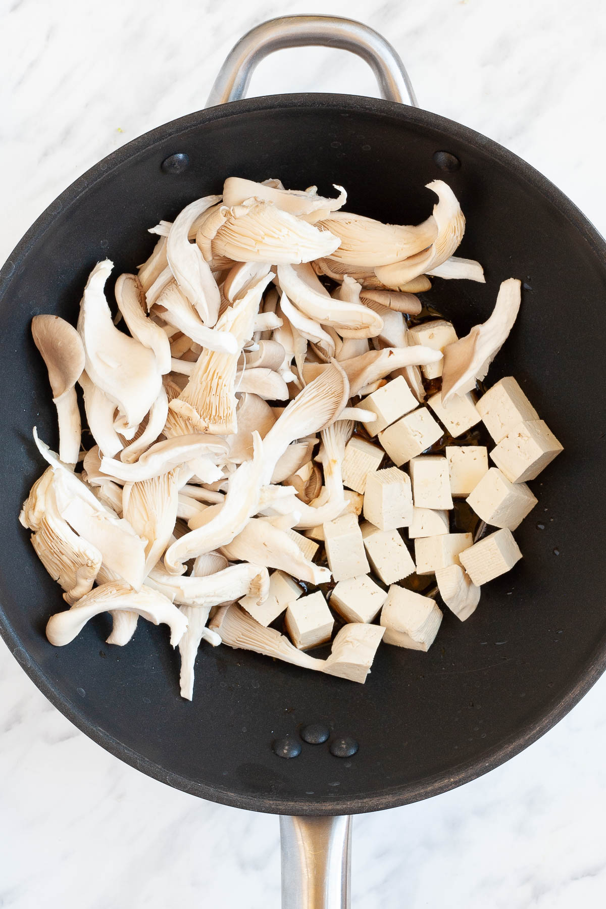 Black wok with mushroom shreds and tofu cubes.