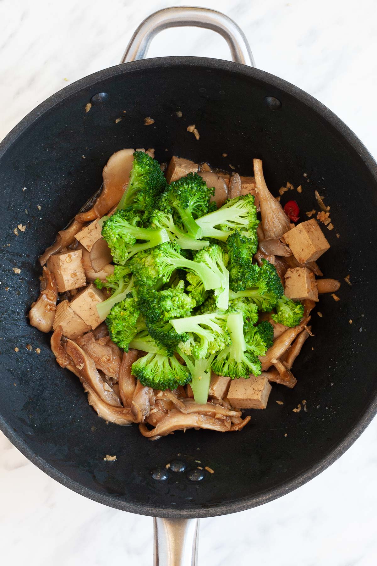 Black wok with mushroom shreds, tofu cubes, broccoli florets brown due to a bit of sauce.